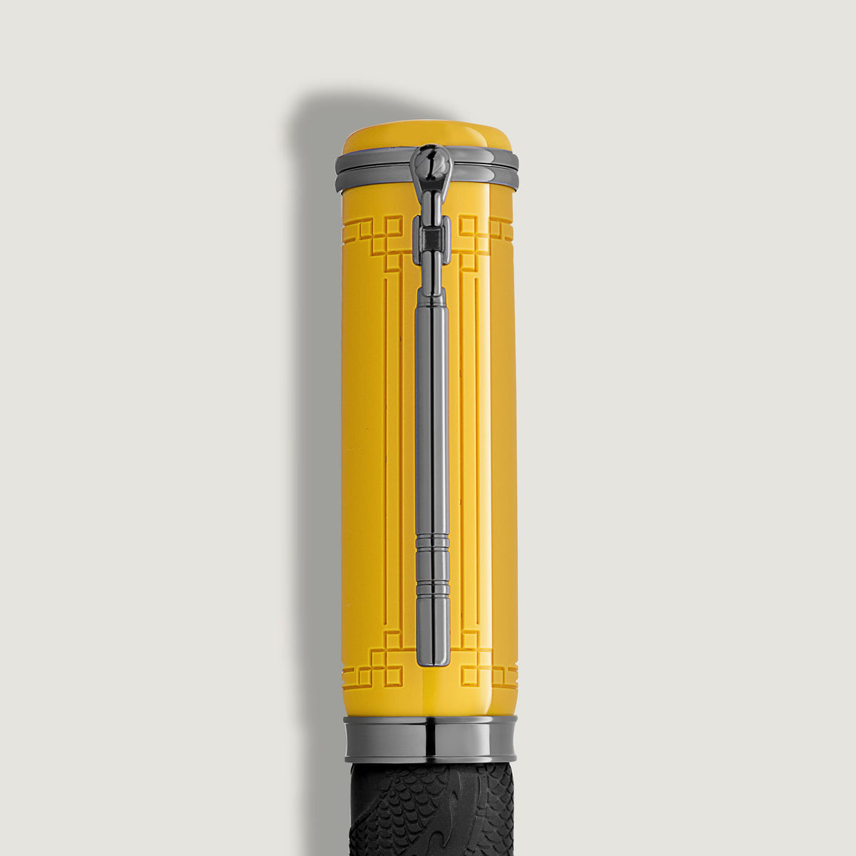 Yellow ballpoint pen cap from the Montblanc Great Characters Bruce Lee Special Edition, featuring a dark metal clip and geometric pattern detail transitioning to a textured black grip.