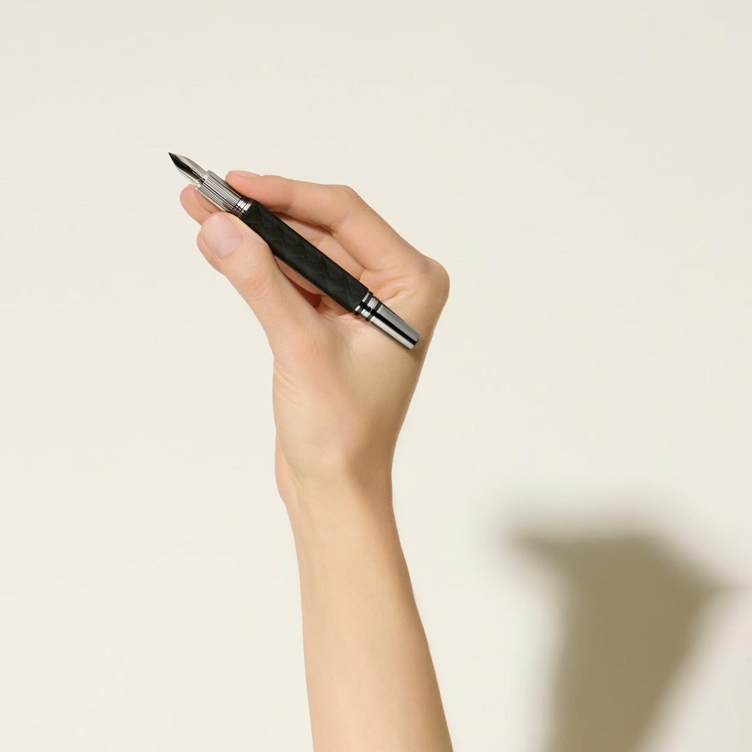A hand holds a Montblanc StarWalker Extreme Precious Resin Fountain Pen with ruthenium-coated fittings against a light background, casting a shadow on the surface.