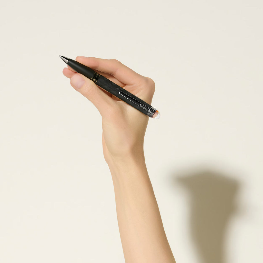 A hand holds the Montblanc StarWalker Extreme Precious Resin Ballpoint Pen, its ruthenium-coated fittings gleaming against a plain light background, with the shadow of this Montblanc writing instrument on the surface.