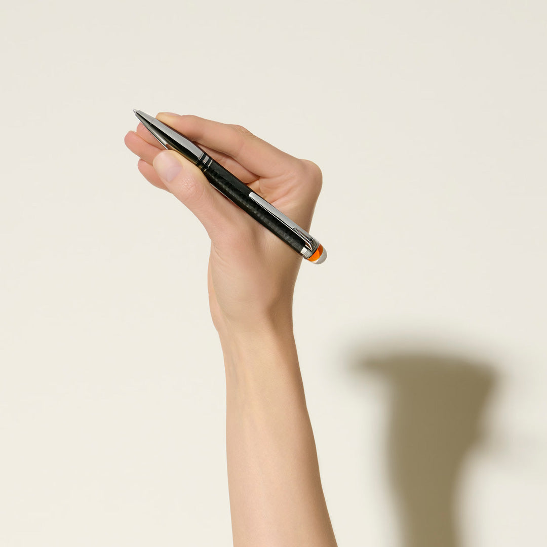 A hand holds the Montblanc StarWalker Extreme Metal Ballpoint Pen upright against a plain light background, its shadow elegantly cast behind. This luxury Montblanc pen features striking ruthenium-coated fittings for a sophisticated look.