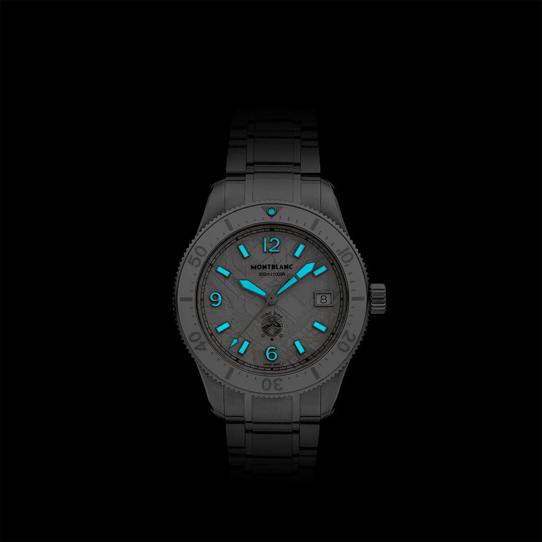 The Montblanc Iced Sea Automatic Date 0 Oxygen 38mm Watch features a metal band, glacier-patterned dial, and glowing blue markers and hands, all set against a solid black background.