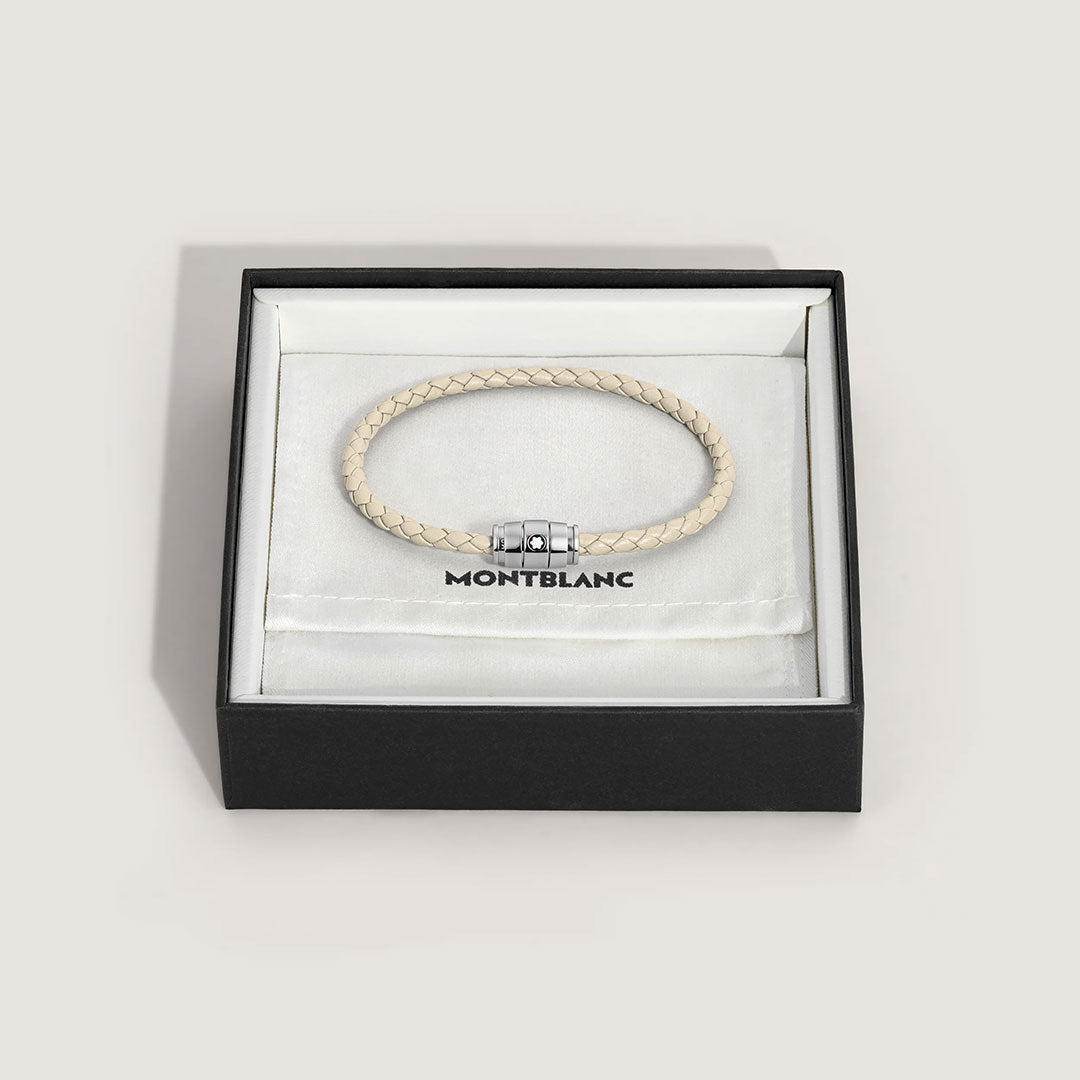 The Montblanc Meisterstuck 3 Rings Cloudy Beige Leather Bracelet, featuring a braided design and magnetic clasp, is displayed in an open black Montblanc box lined with white fabric.