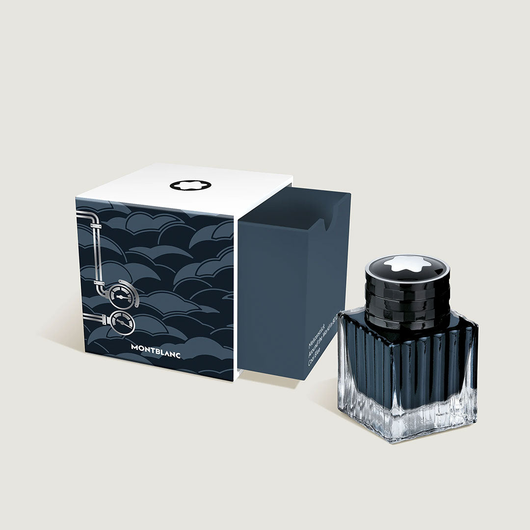 The Montblanc Meisterstück Around the World in 80 Days Coal Blue 50ml ink comes in a clear, faceted bottle with a black cap, presented next to its decorative box—a stylish Special Edition collectible by Montblanc.