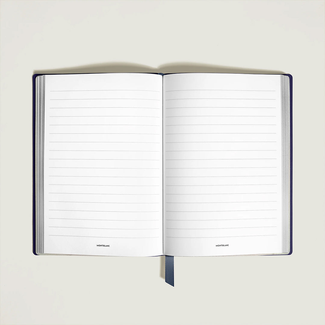 The Montblanc Meisterstuck Around the World in 80 Days Notebook, featuring medium lined pages and a dark blue bookmark, lies flat against a plain background, highlighting its compact design.