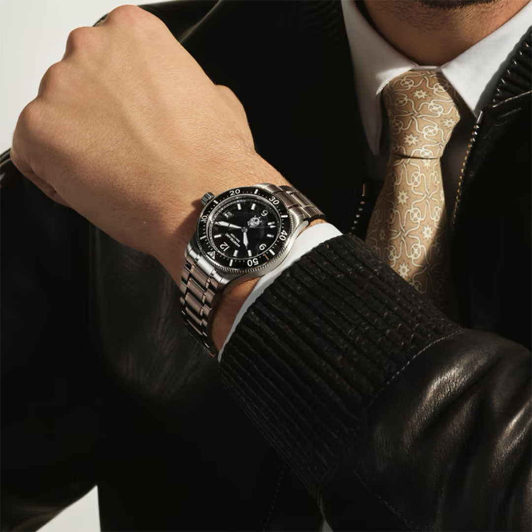 A person in a black leather jacket and patterned tie showcases the Montblanc Iced Sea Automatic Date 0 Oxygen 38mm Watch with a striking black glacier dial on their bent left wrist, highlighting the timepiece.