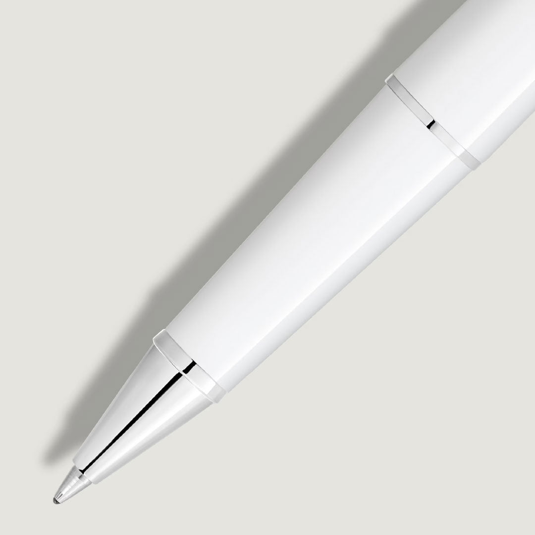 A close-up of the Montblanc Meisterstuck White Classique Rollerball Pen, featuring platinum-coated accents, rests on a light grey surface and casts a soft shadow to the left.