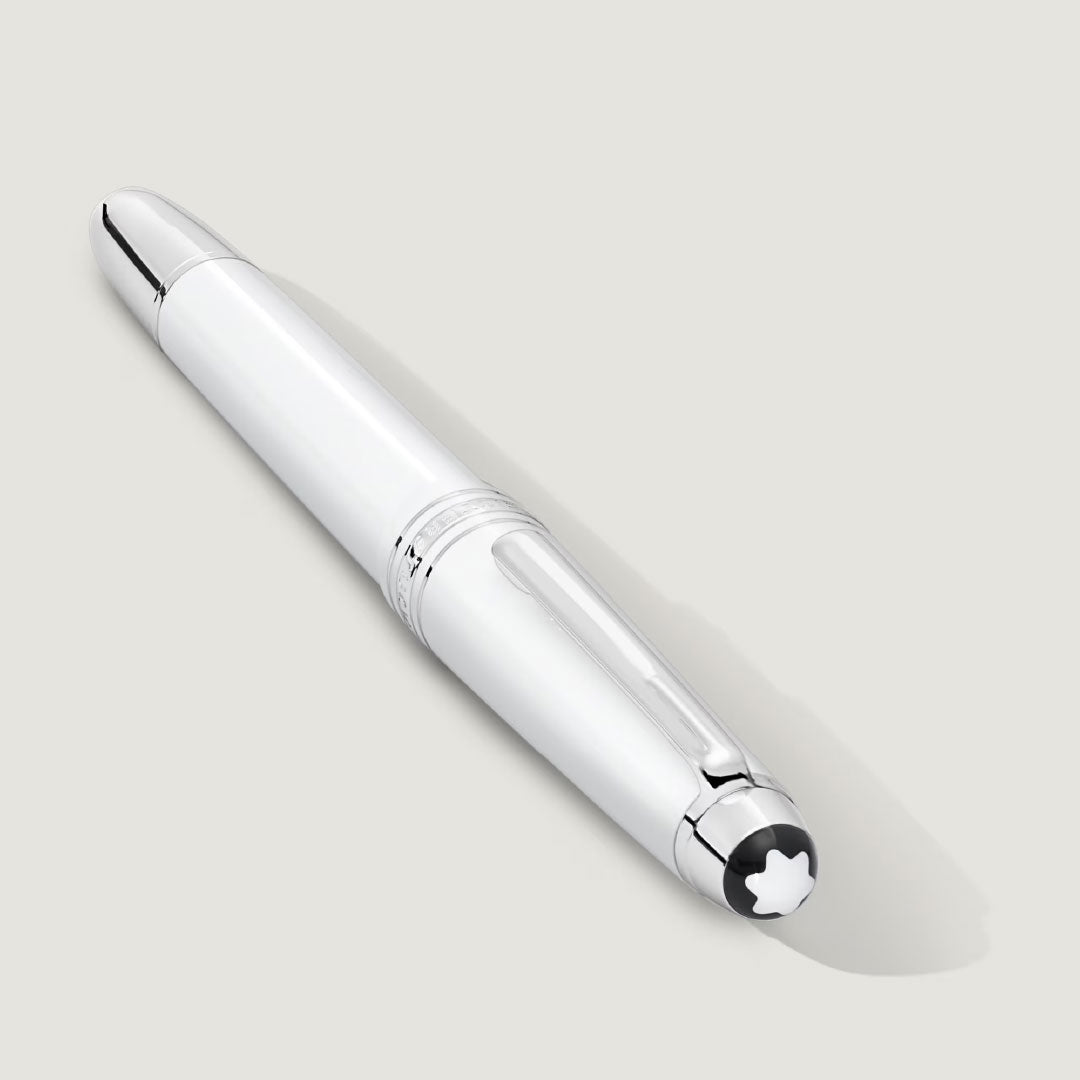 A Montblanc Meisterstuck White Classique Rollerball Pen with platinum-coated silver accents rests diagonally on a light gray surface, its cap featuring Montblanc’s signature white star emblem in a black circle.