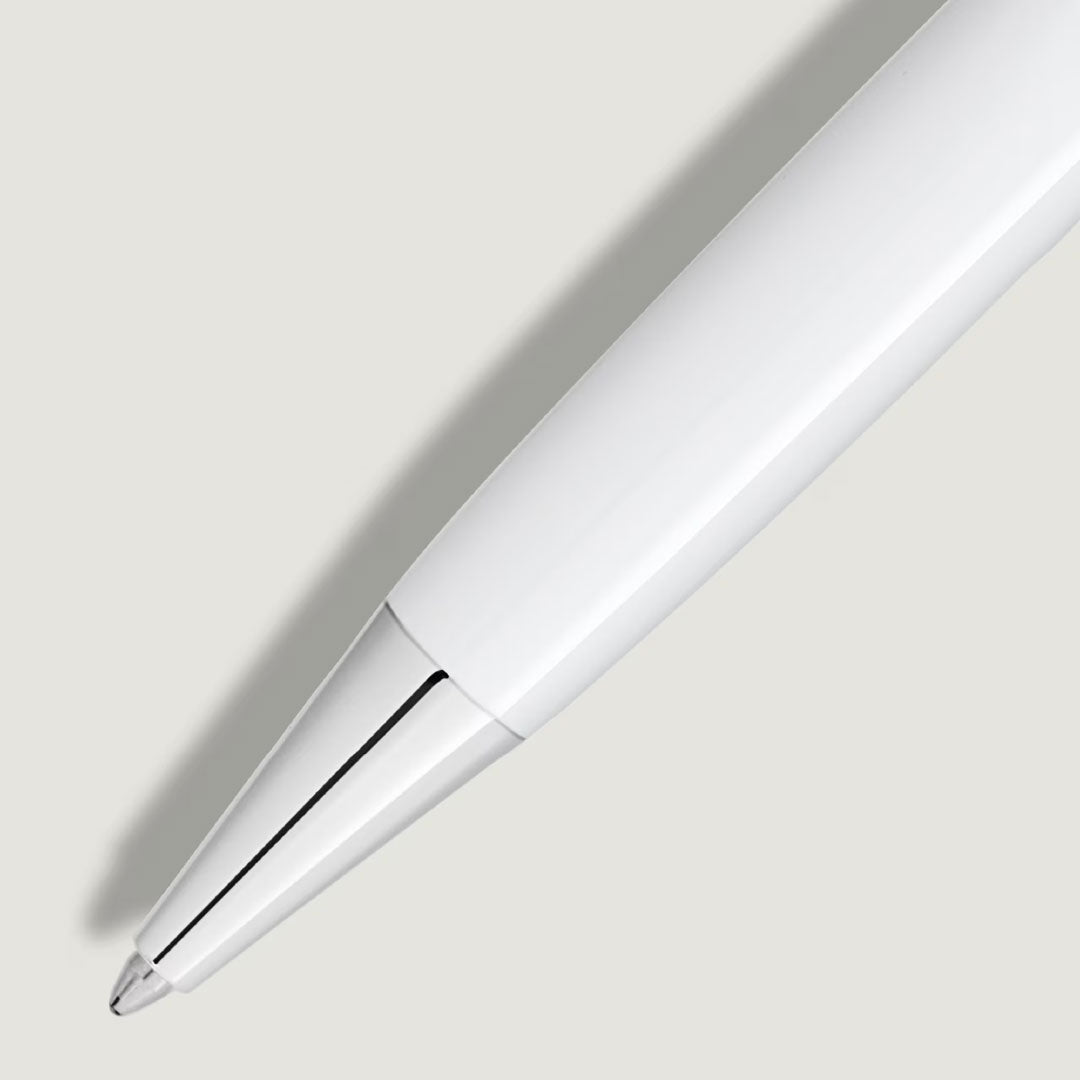 A close-up of the Montblanc Meisterstuck White Classique Ballpoint Pen shows its platinum-coated fittings and silver tip, positioned diagonally on a light gray background and casting a soft shadow to the left.
