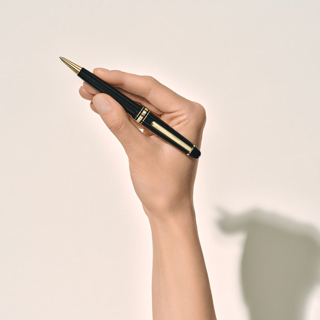 A hand holds a Montblanc Meisterstuck Ballpoint Pen by Montblanc against a light background, with the shadow of the hand and pen cast on the surface.
