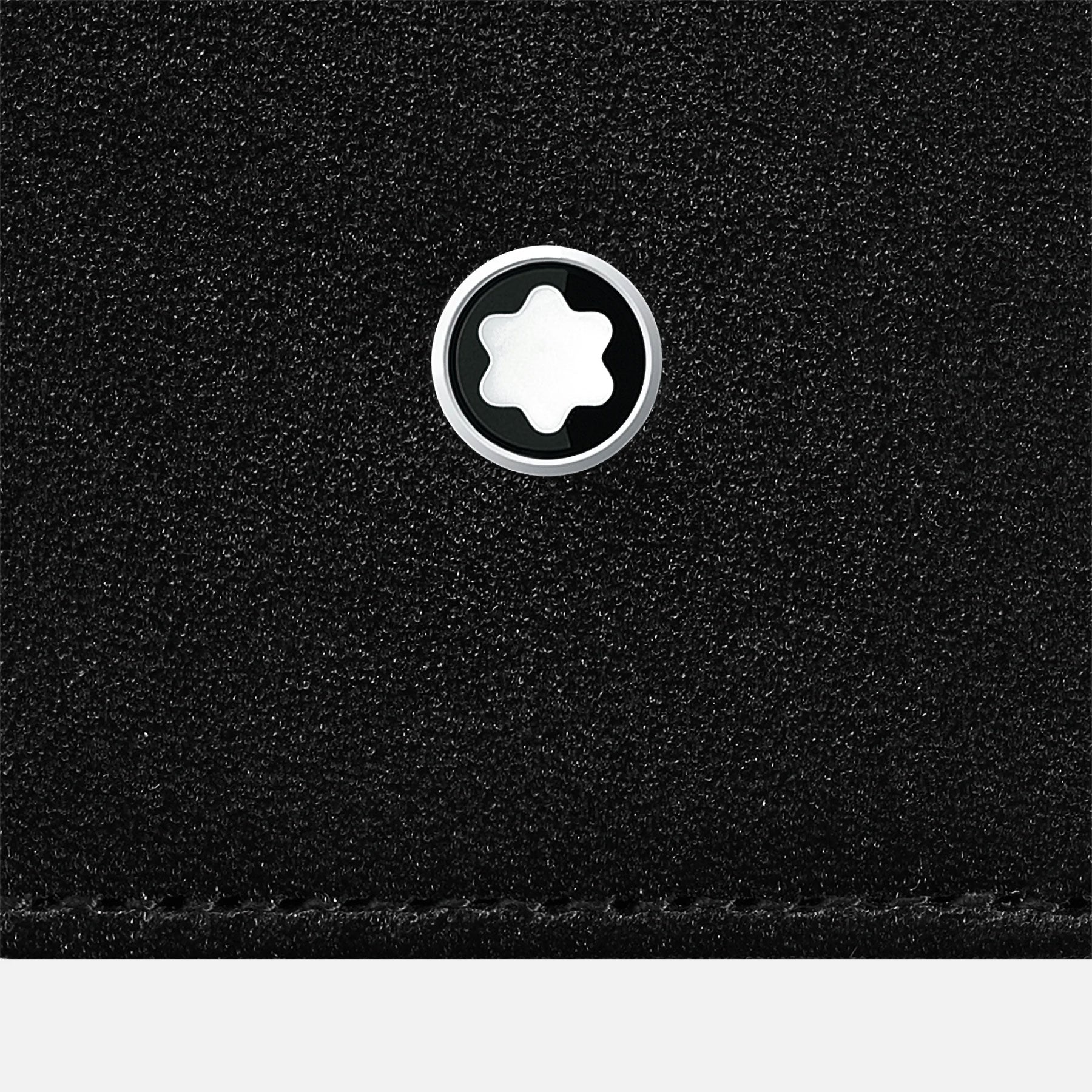 A close-up of the textured black leather surface of the Montblanc Meisterstück Black Leather Pen Pouch highlights a silver and black circular Montblanc emblem at its center, with a star-like shape within the emblem, capturing the elegance typical of Montblanc's design.