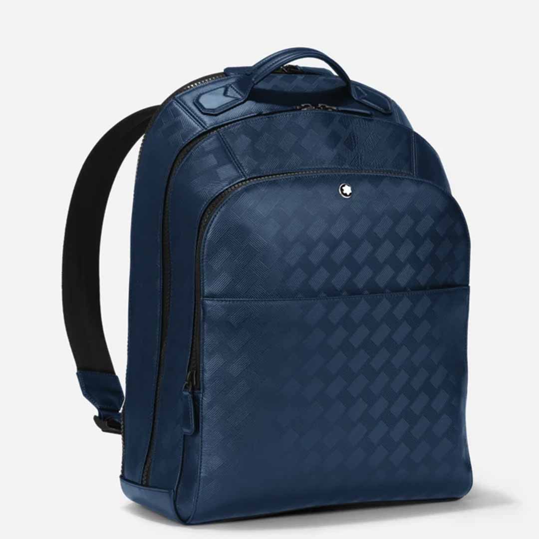 The Montblanc Extreme 3.0 Blue Leather Backpack, designed by Montblanc, showcases a stylish dark blue full-grain leather construction with a subtle checkered pattern. It features a front zip pocket, top handle, and adjustable black shoulder straps, all displayed against a plain white background.
