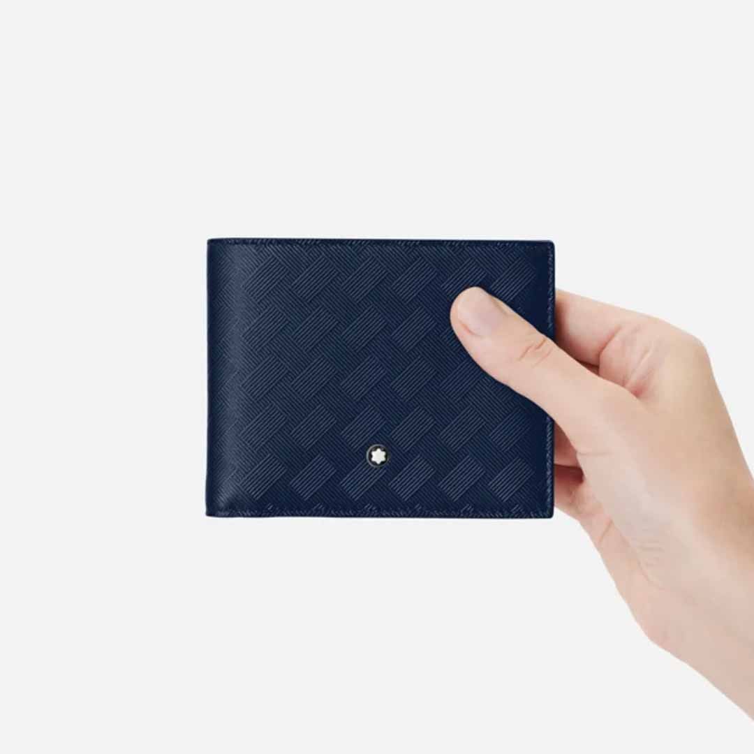 In a hand rests the Montblanc Extreme 3.0 Blue 6cc Leather Wallet, showcasing its full-grain bovine leather construction with a textured pattern and a small silver emblem adorning the front. Inside, thoughtfully arranged credit card slots enhance its practicality. The light-colored background provides an elegant contrast to this refined accessory from Montblanc.