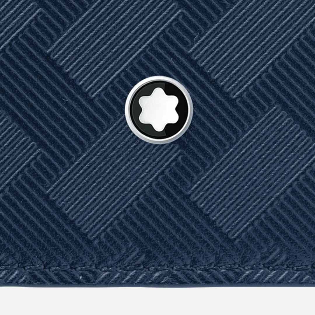 Close-up of a dark textured surface with a herringbone pattern, featuring a circular metallic emblem in the center with a white star-shaped design, reminiscent of the Montblanc Extreme 3.0 Blue 6cc Leather Wallet crafted from full-grain bovine leather by Montblanc.