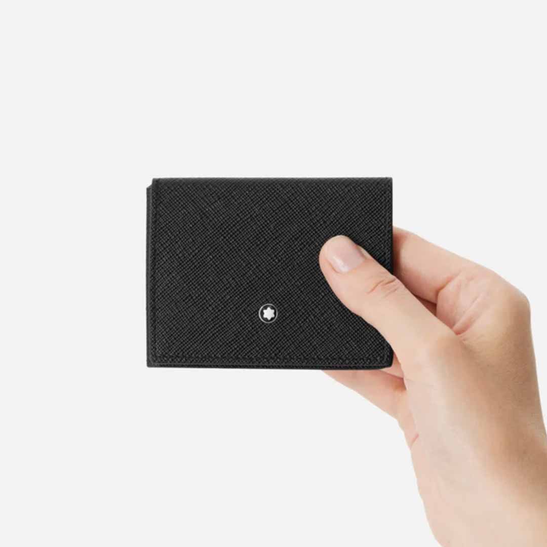 A hand holding the elegant Montblanc Sartorial Trio 4cc Leather Card Holder made of sleek, black saffiano leather with a minimalist design against a white background. The tri-fold card holder from Montblanc features a small, circular emblem on the front and multiple credit card slots inside for convenience.