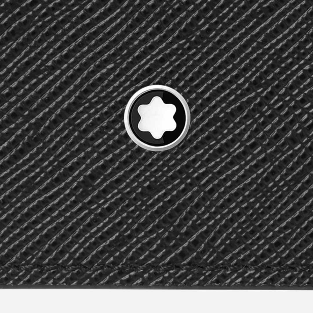 Close-up of the textured black saffiano leather surface of the Montblanc Sartorial Trio 4cc Leather Card Holder, featuring a circular silver emblem with a white six-pointed star at its center. The surface showcases a fine diagonal striped pattern typical of tri-fold card holders with credit card slots, by Montblanc.