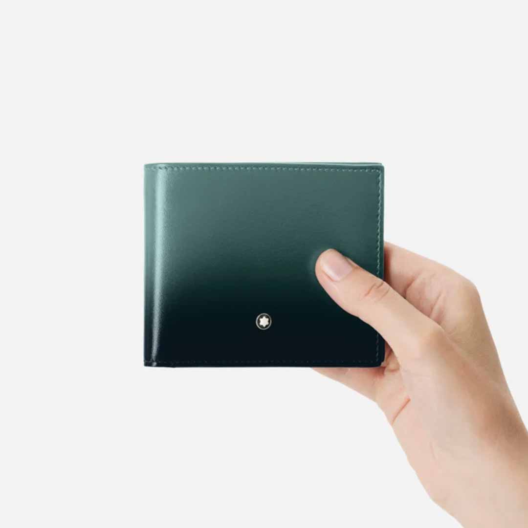 A hand holds a closed Montblanc Meisterstück 6cc Leather Wallet, crafted from premium British green leather, against a plain white background. The wallet showcases a small circular metal logo on the front, blending elegance and sophistication with an artful sfumato effect.