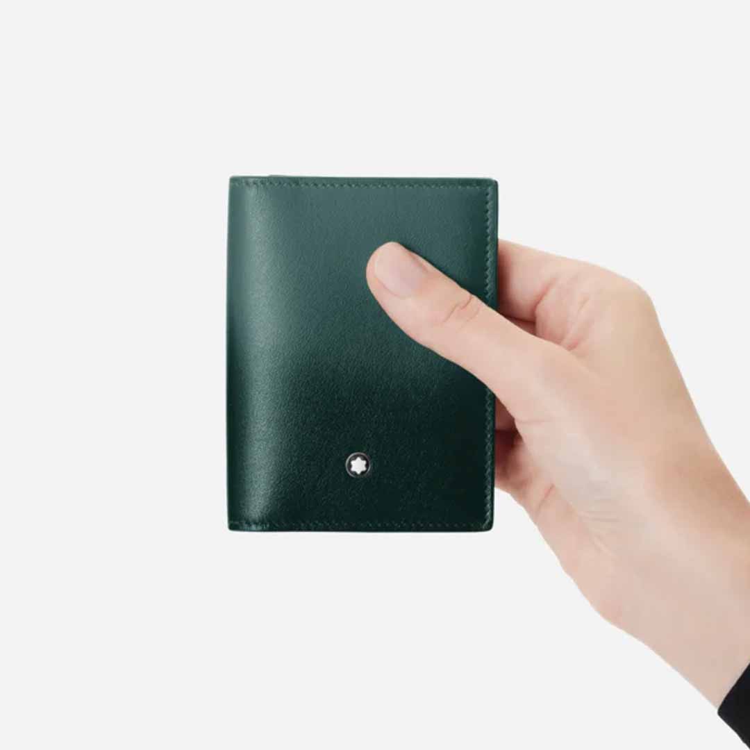 A hand holding the elegant Montblanc Meisterstück 4cc Leather Card Holder, crafted from luxurious British green leather and featuring a logo emblem on the corner. The plain white background accentuates this piece from Montblanc's exclusive 100 Years collection, highlighting its sophisticated design.