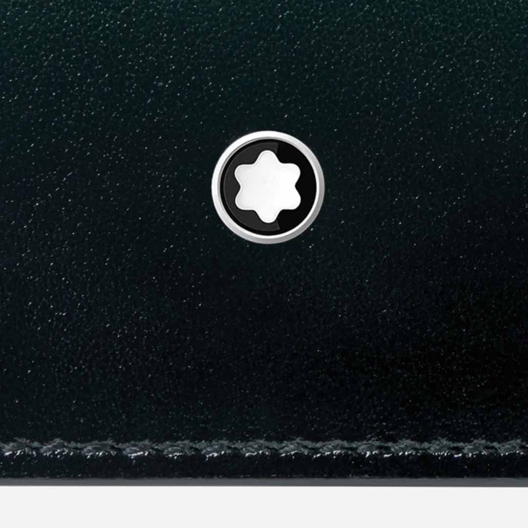 A close-up view showcases the British green leather surface of the Montblanc Meisterstück 6cc Leather Card Holder. In the center, a small, circular metallic emblem with a distinctive white star-shaped design catches the eye. The bottom edge features neat stitching along the leather, embodying the timeless elegance that defines Montblanc's Meisterstück card holder collection.