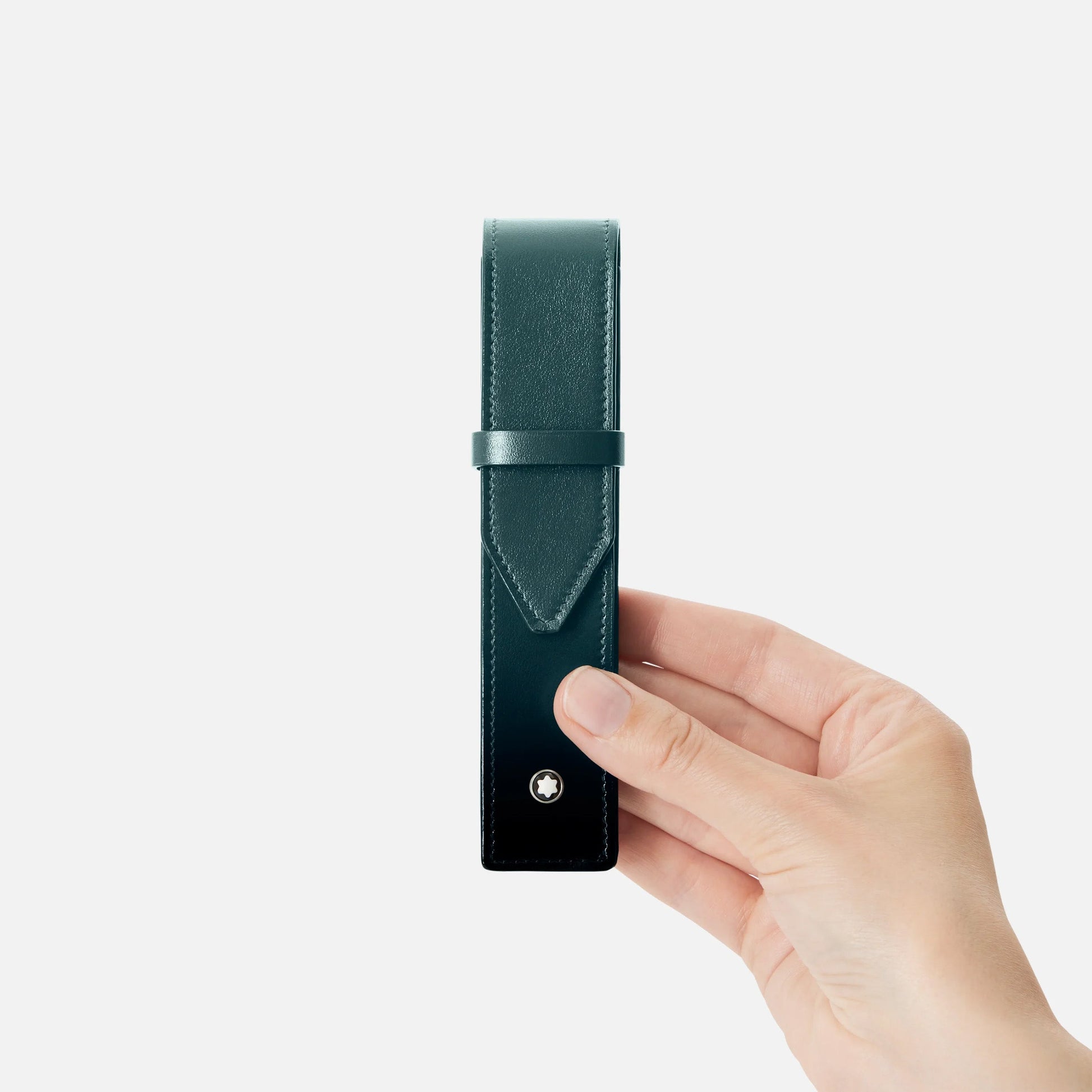 A hand holds the elegant Montblanc Meisterstück Single Pen Pouch in British green leather, featuring a flap with a small circular metal button. The plain white background accentuates this stylish writing instrument case from Montblanc.