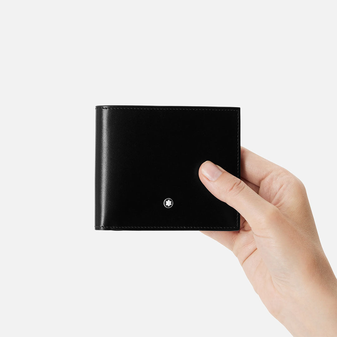 A hand holds a closed Montblanc Meisterstuck 6CC Leather Wallet featuring a small circular metal emblem on the front, set against a plain white background.