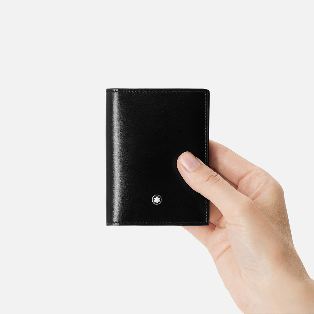 A hand holds a Montblanc Meisterstuck 4CC Leather Card Holder in black, featuring a small round silver Montblanc emblem near the bottom center, set against a plain white background.