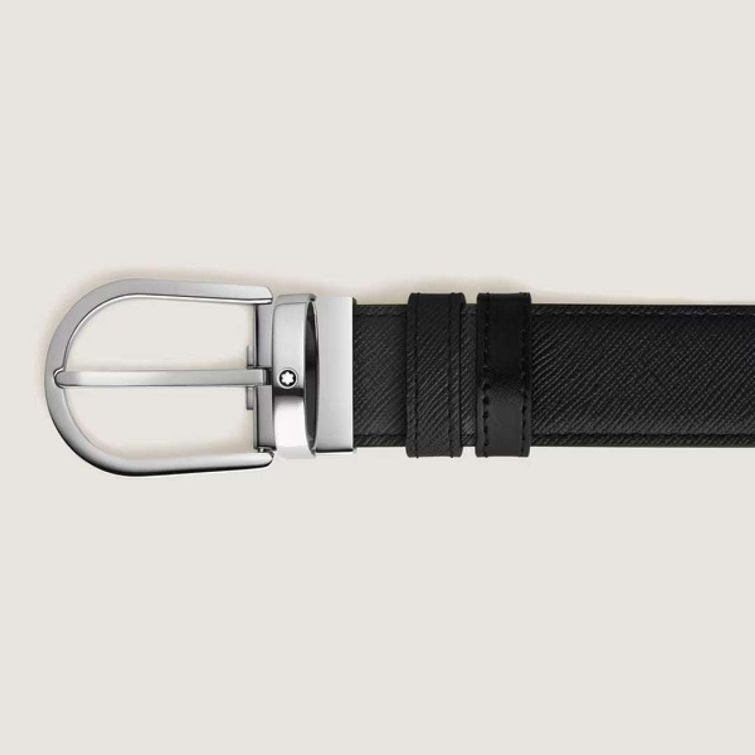 The Montblanc Horseshoe Buckle 35mm Reversible Leather Belt, crafted from black saffiano-printed leather with a textured finish and a shiny Montblanc horseshoe buckle, is displayed horizontally on a light beige background.