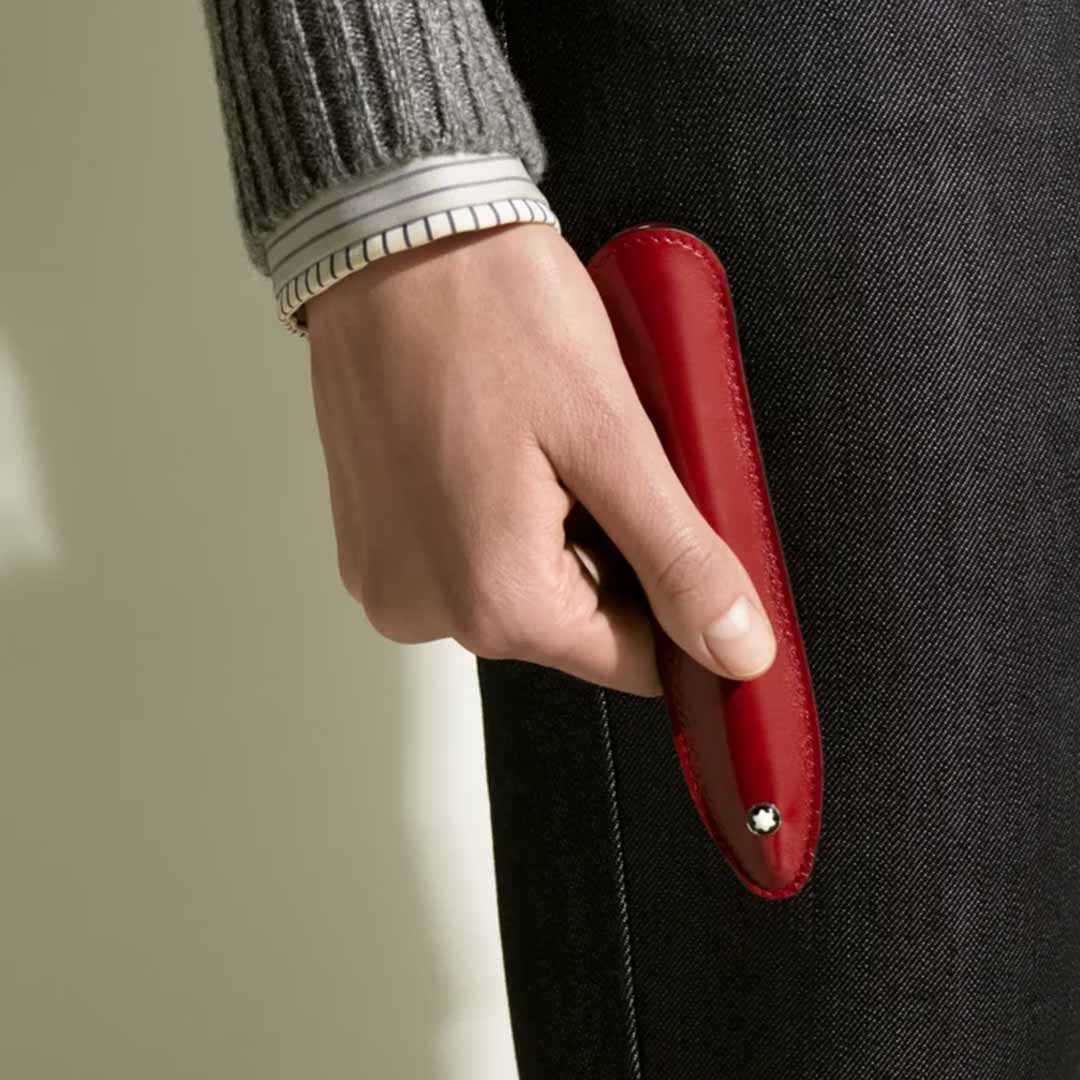 The Montblanc Sartorial Single Writing Instrument Sleeve is a red accessory crafted from Saffiano leather, featuring a textured yet smooth surface. It has a rounded top with a tapered bottom and displays a small white emblem near the base.