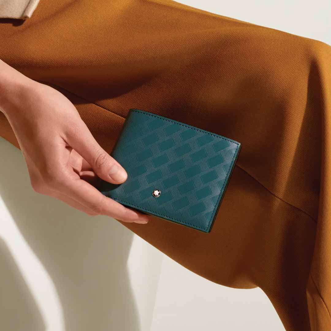 A person holds a Montblanc Extreme 3.0 6cc Leather Wallet with a textured pattern, placed on a brown skirt. The wallet showcases the Montblanc emblem at its bottom corner, creating a striking contrast against the neutral light background.