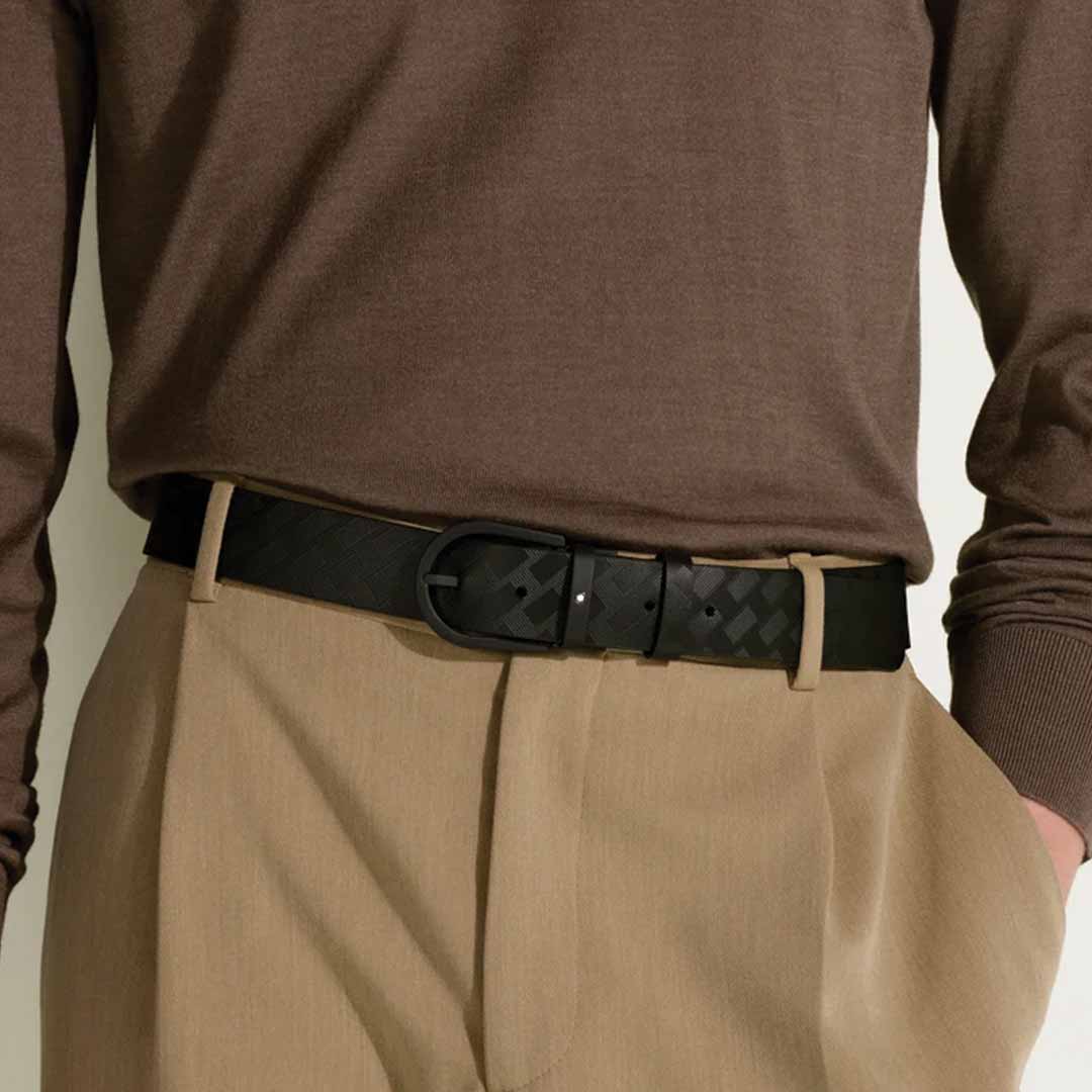 A person is dressed in a brown long-sleeve shirt tucked into beige trousers, accentuated with the Montblanc Horseshoe 35mm Leather Belt. The emphasis is on the waist area, showcasing the belt's distinctive buckle.
