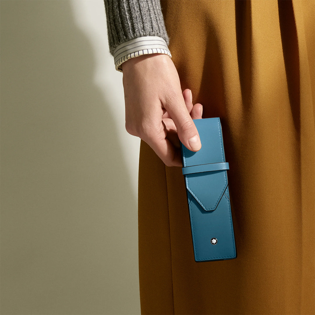 A person in a grey sweater and mustard-yellow skirt holds a Montblanc Meisterstück Leather Double Pen Pouch against a neutral background.