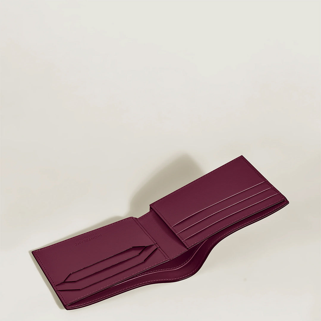 The Montblanc Meisterstuck 6CC Wallet, crafted in cassis leather, displays a maroon bi-fold design with multiple card slots on each side. Featuring the subtle Montblanc emblem, it rests elegantly against a plain, light background.