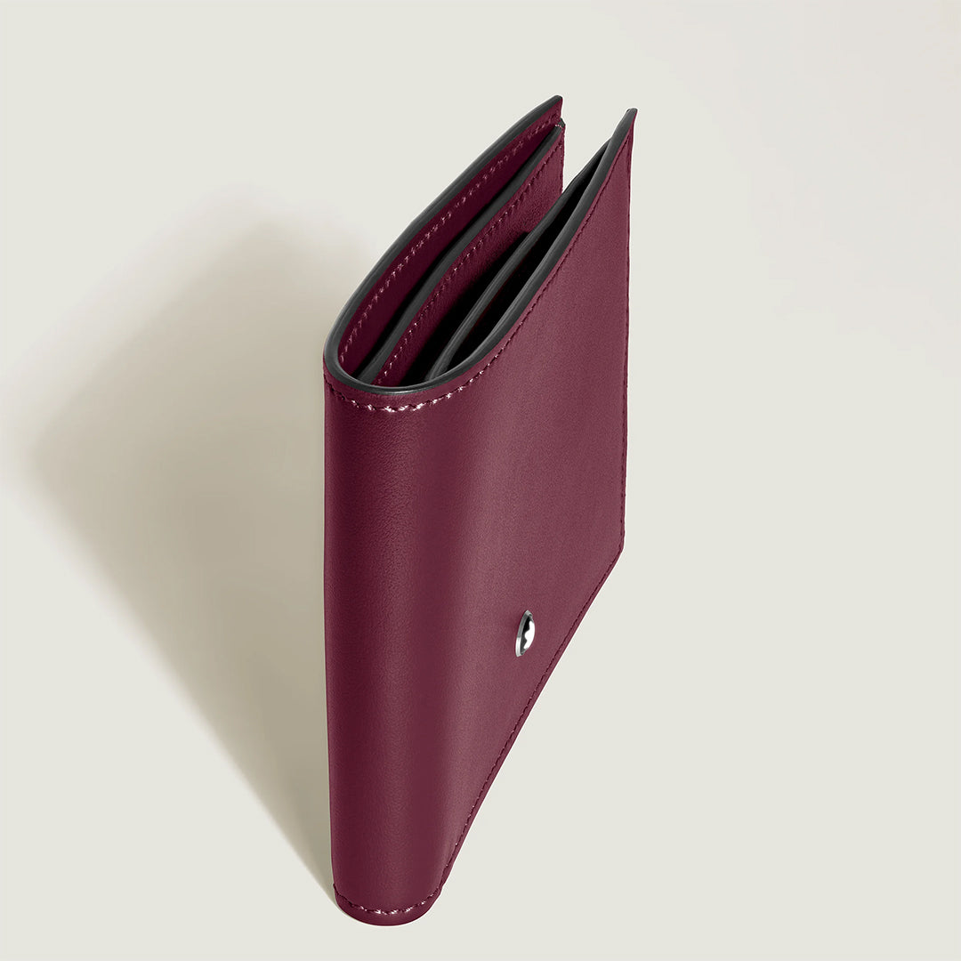 The Montblanc Meisterstück 6CC Wallet in burgundy cassis leather is displayed upright, highlighting its sleek profile. The smooth finish and partially open design reveal inner credit card slots against a simple light backdrop.