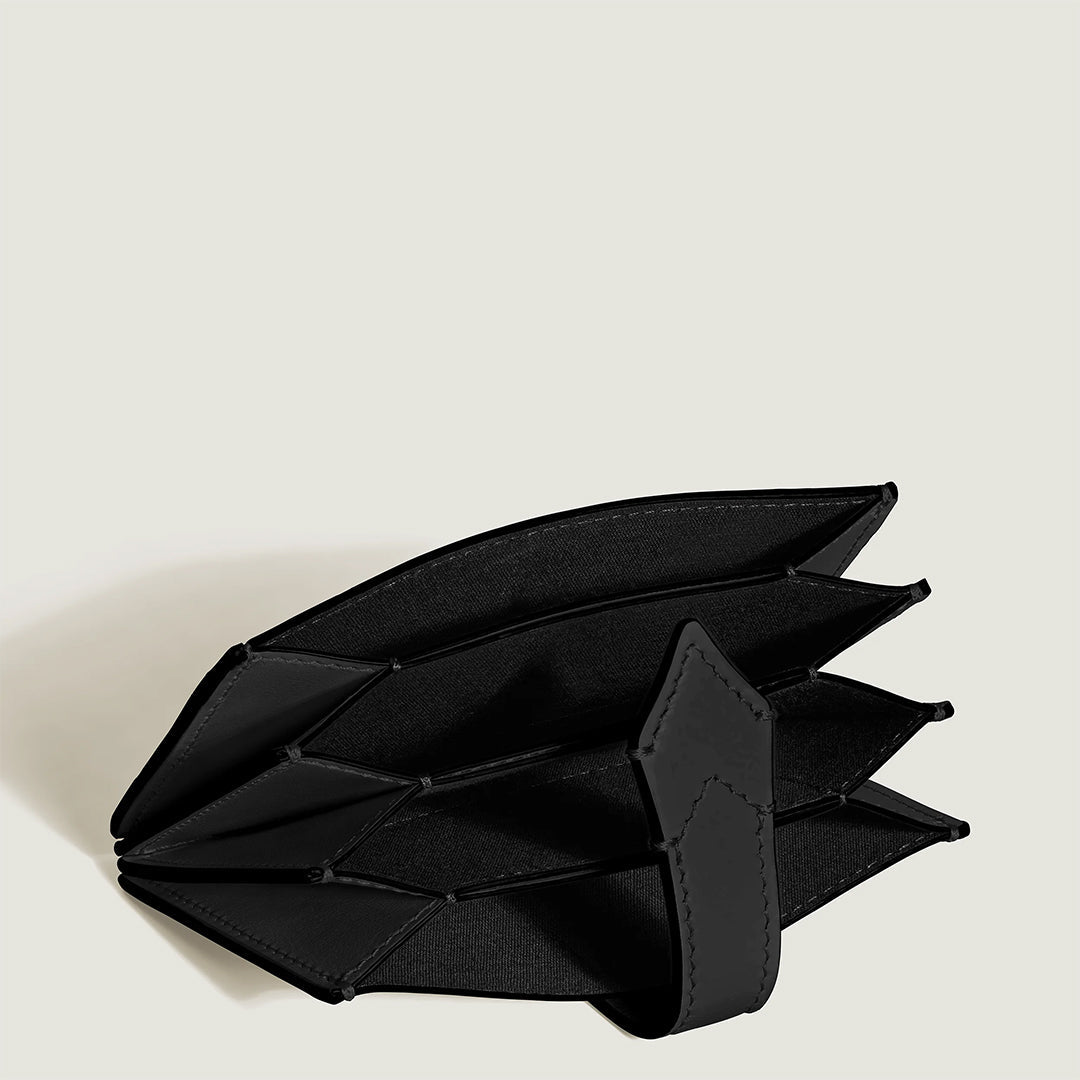 The Montblanc Meisterstuck 5CC Card Holder, crafted from sleek black leather, is open against a white backdrop. This modern card holder with an accordion-style design and strap reveals its spacious, organized interior by showcasing multiple compartments for holding items.