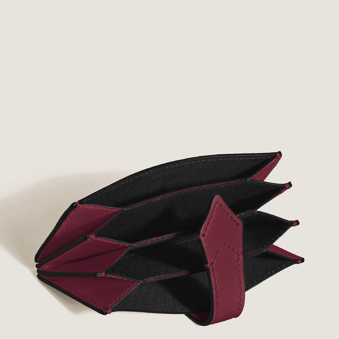 The Montblanc Meisterstuck 5CC Card Holder, crafted from textured cassis leather in maroon and black, features an open accordion design with multiple compartments. It showcases Montblanc's signature style and a strap closure against a plain white backdrop.