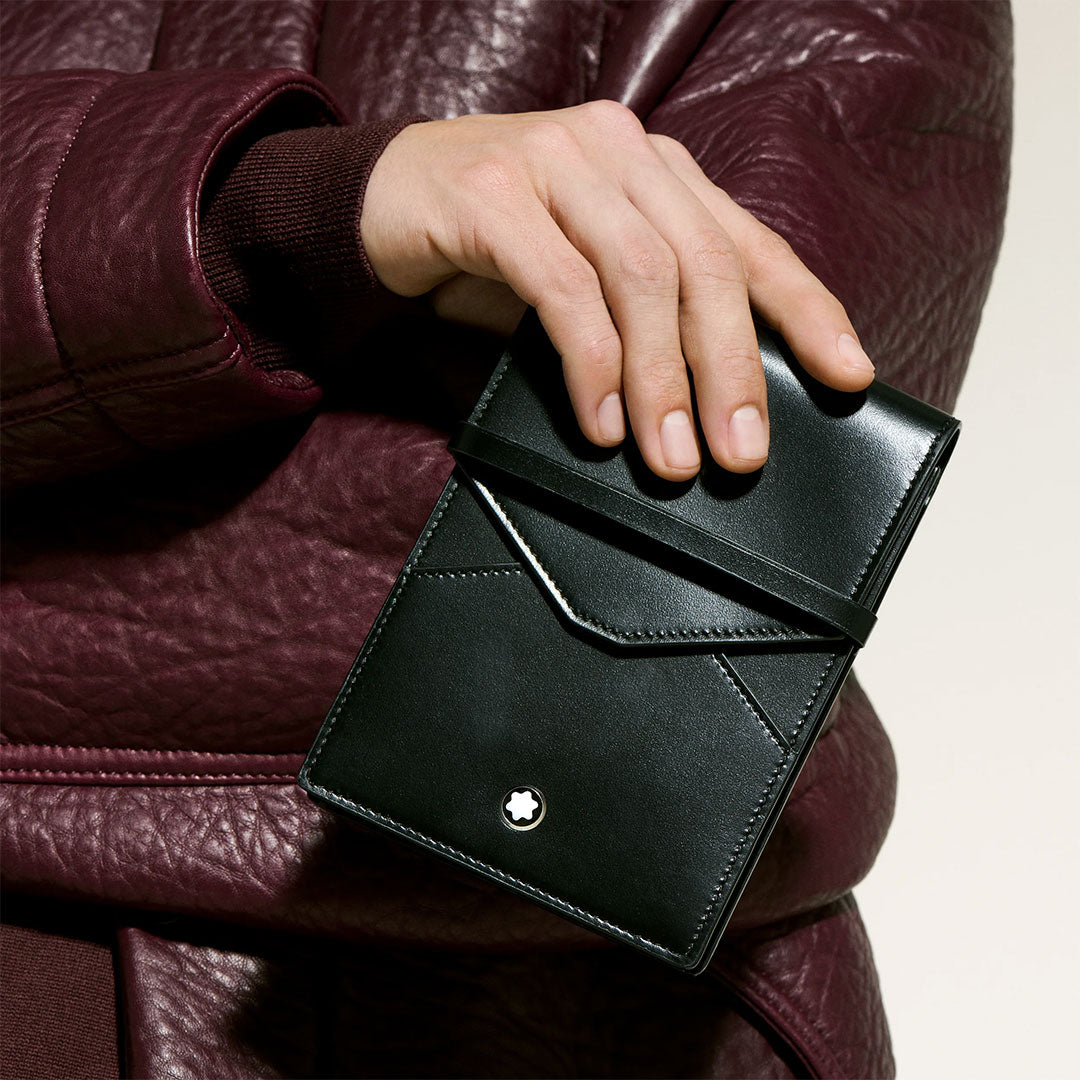 A person wearing a burgundy leather jacket holds a sleek black Montblanc Meisterstuck 5 Pen Leather Pouch, featuring the Montblanc emblem on the front and designed to securely hold multiple writing instruments.