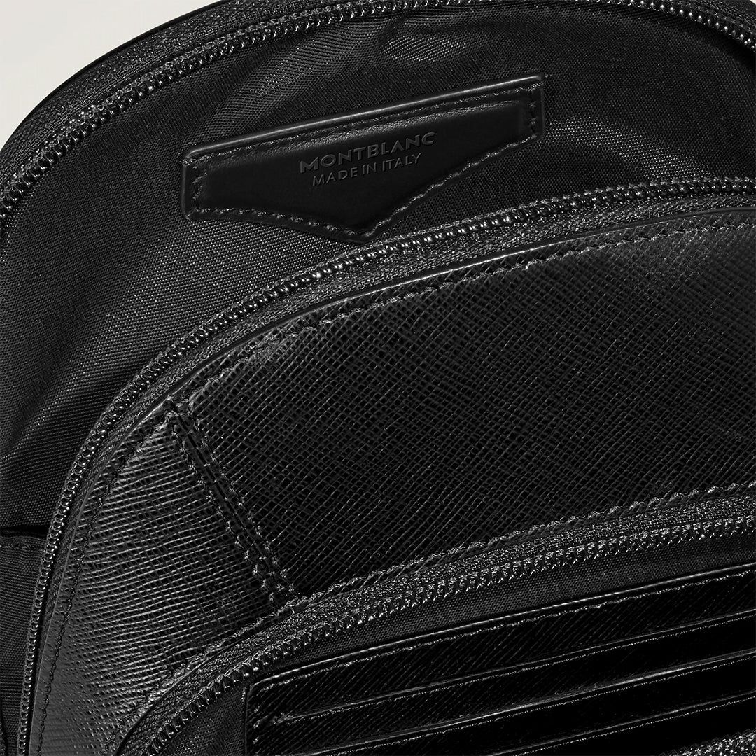 Close-up of a Montblanc Sartorial Sling Bag showcasing its black leather, a "Montblanc Made in Italy" label, and partially open zip that reveals the textured Saffiano-embossed surface and intricate stitching, blending elegance with craftsmanship.