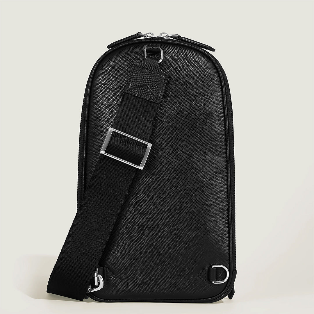 The Montblanc Sartorial Sling Bag is crafted from Saffiano-embossed leather with a textured black surface. It features an adjustable shoulder strap with sleek silver buckles and hardware, set against a light gray background.