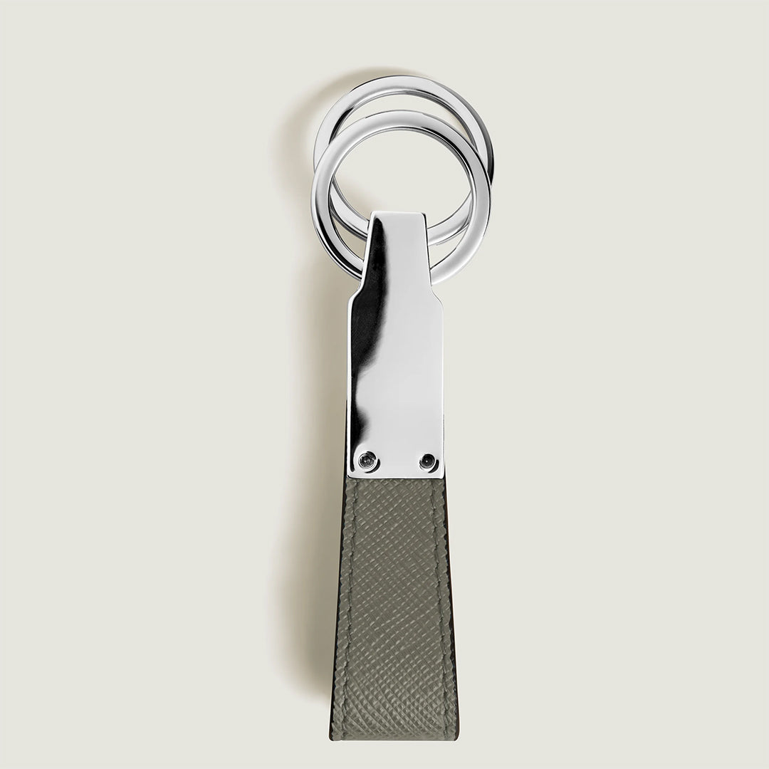 The Montblanc Sartorial Loop Key Fob features three silver rings, one detachable, and a textured rectangular Saffiano leather strap, displayed vertically against a plain light background.