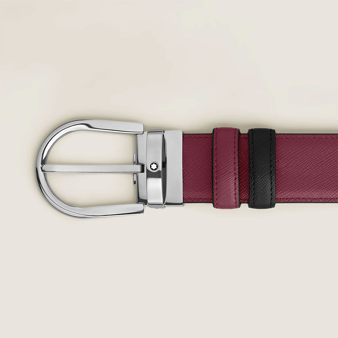 A close-up of the Montblanc Horseshoe Buckle 35mm Reversible Leather Belt, featuring burgundy calfskin leather, a silver buckle, and a black leather loop, displayed against a light beige background.
