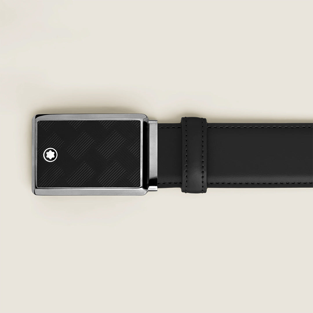 The Montblanc 35mm Black Leather Belt features a stylish plate buckle with a textured pattern and the Extreme 3.0 motif as a small circular emblem. Laid flat on a light beige background, it exudes understated elegance.