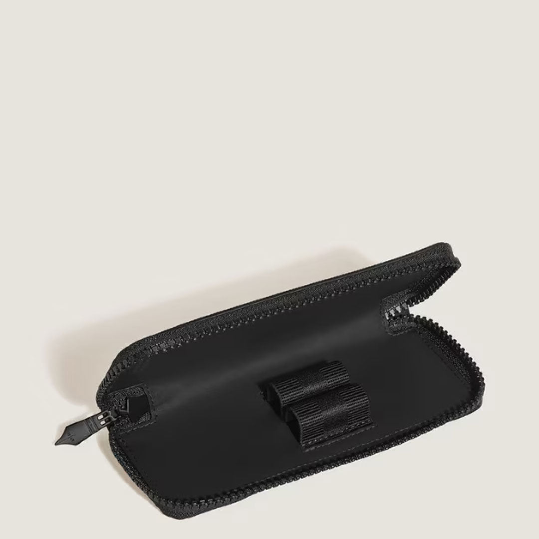 The Montblanc Extreme 3.0 Black Leather Double Pen Pouch by Montblanc sits open on a beige surface, showing its empty interior with two elastic loops designed to securely hold pens or other small items.