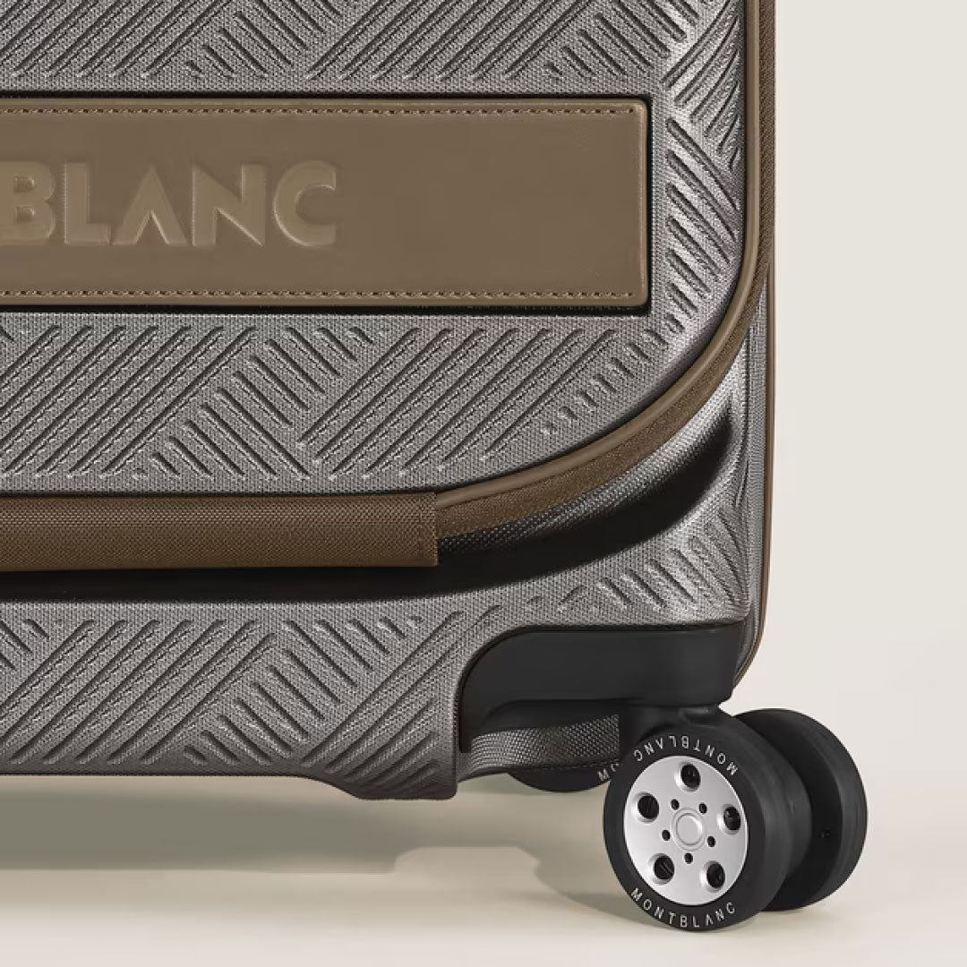 Close-up of the Montblanc Extreme 3.0 Cabin Luggage with Pocket, featuring textured metallic polycarbonate, brown accents, a leather panel embossed with "BLANC," and a wheel labeled "Montblanc.