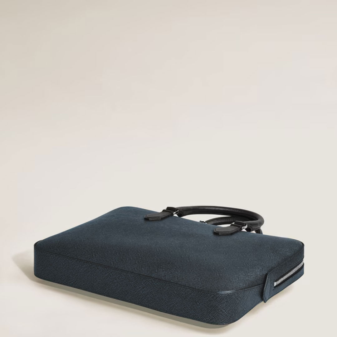 A Montblanc Sartorial Thin Document Case Bag in dark blue leather with black handles sits at an angle on a plain, light surface.