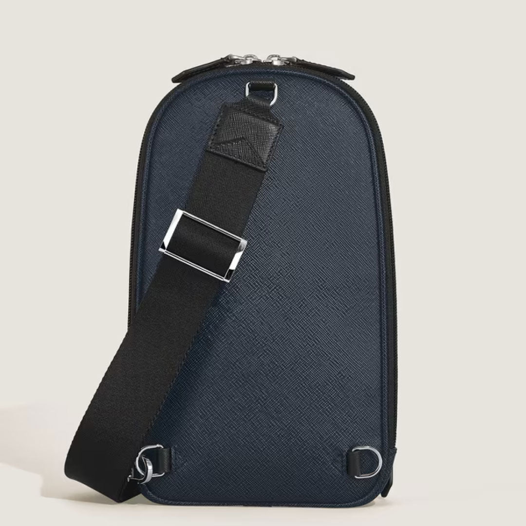 The Montblanc Sartorial Leather Sling Bag, in dark blue with a textured finish, features a black adjustable shoulder strap and silver hardware, shown upright against a plain light background.