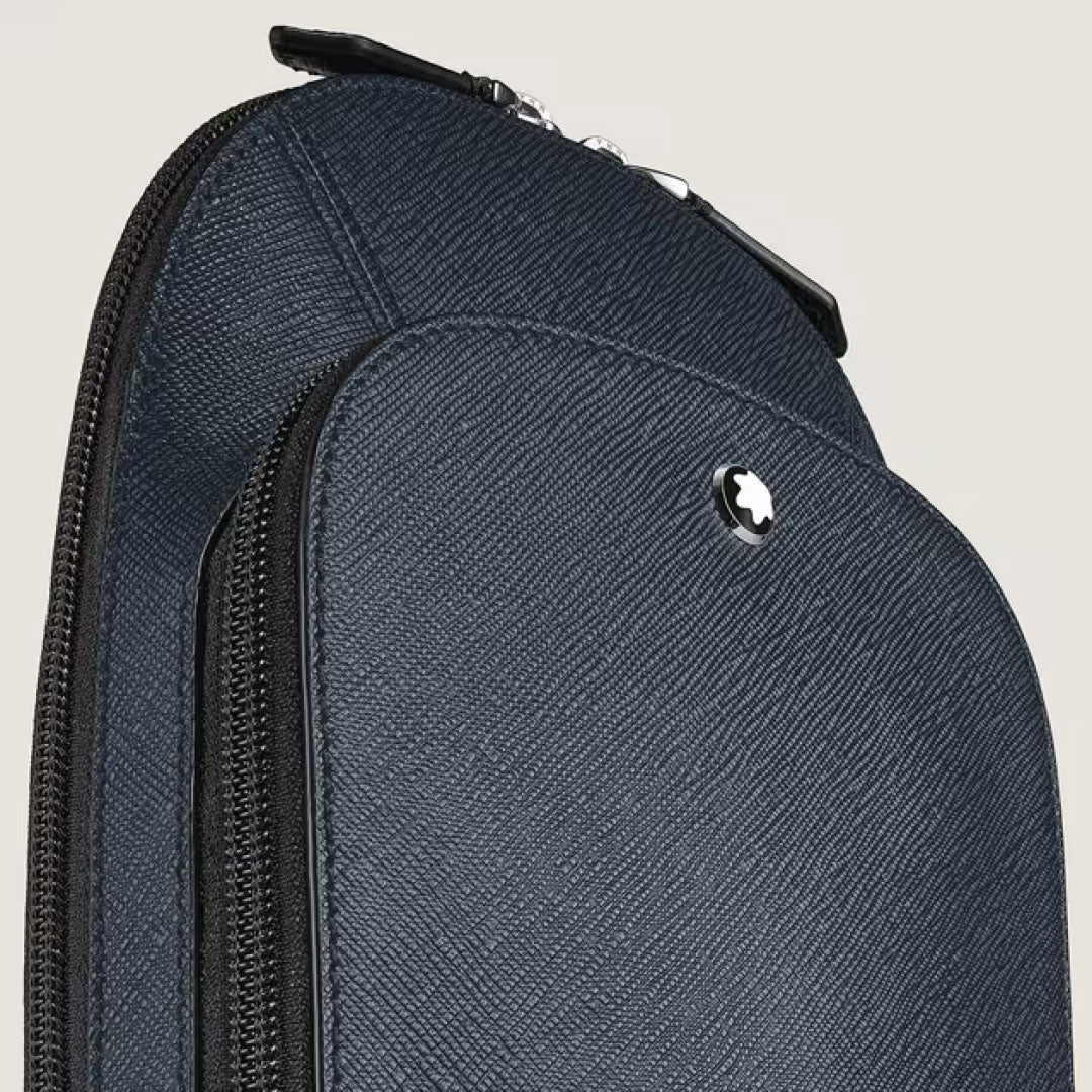 Close-up of the Montblanc Sartorial Leather Sling Bag, featuring dark textured leather, a zipper, and Montblanc's signature round silver emblem near the top, set against a plain light background.