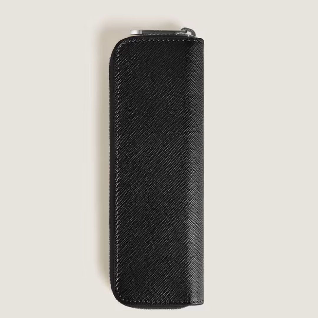 The Montblanc Sartorial Single Leather Pen Pouch with Zip, crafted from black textured leather with white stitching, features a slim rectangular design and stands vertically against a light beige background.