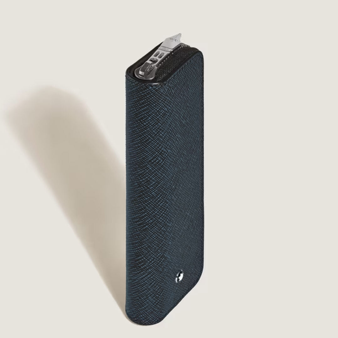 The Montblanc Sartorial Blue Single Leather Pen Pouch with Zip stands upright on a light background, partly open to reveal a silver Montblanc pen inside. A small circular Montblanc emblem is near the bottom.