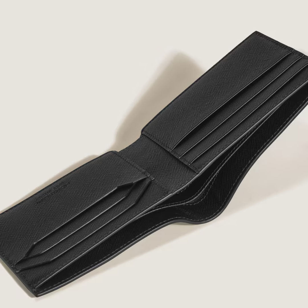 The Montblanc Sartorial Leather 6cc Wallet in black is open to reveal multiple card slots and compartments, elegantly displayed on a light beige surface.