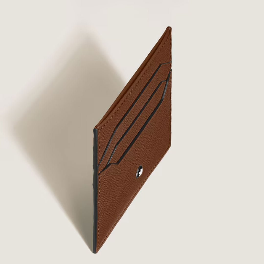 The Montblanc Sartorial Leather 6cc Card Holder by Montblanc stands upright on a light beige surface, casting a shadow to the left.
