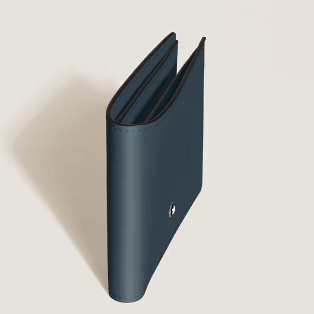 A Montblanc Meisterstuck 6CC Leather Wallet in dark blue stands upright, partially open, on a light beige surface, showing a small circular metal emblem on the front.